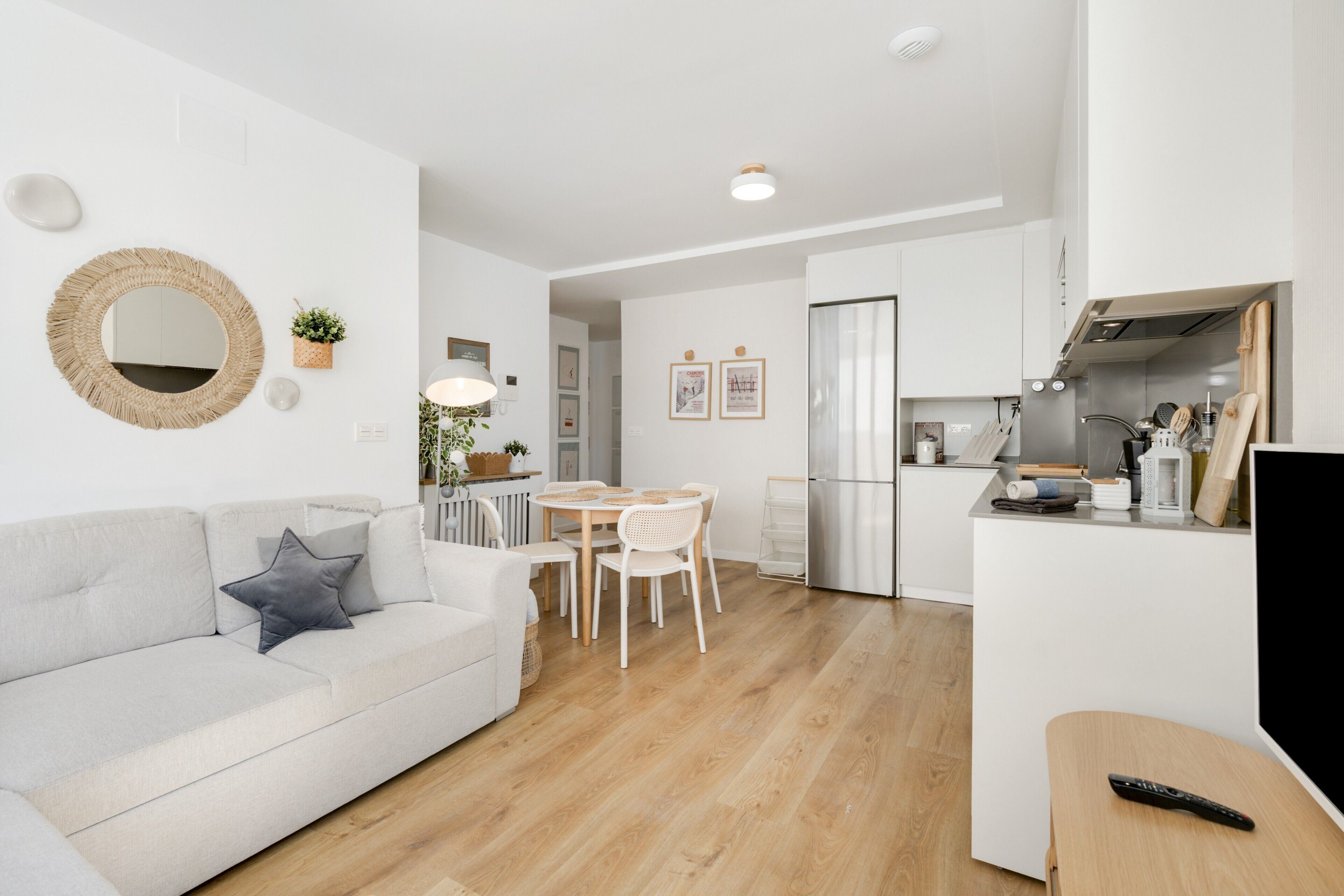 Ein modernes Wohnzimmer mit Sofa, Esstisch und Stühlen, eine Küche mit Kühlschrank und Herd, sowie ein Fernseher auf einem Schrank.
