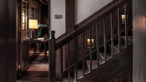 Μια ξύλινη σκάλα με ένα χέρι για στήριξη, ένα γραφείο με ένα φωτιστικό και μια πόρτα με την επιγραφή «101» σε έναν διάδρομο με πλακάκια στο δάπεδο.