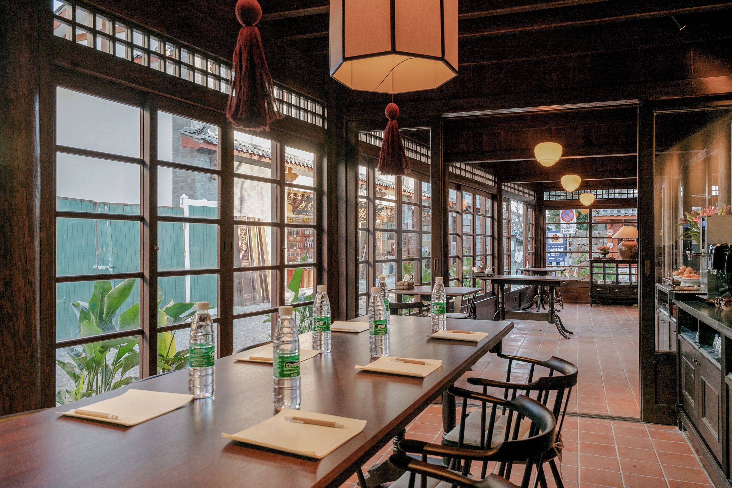 Een restaurant met grote ramen, houten tafels, stoelen en hangende lampen.