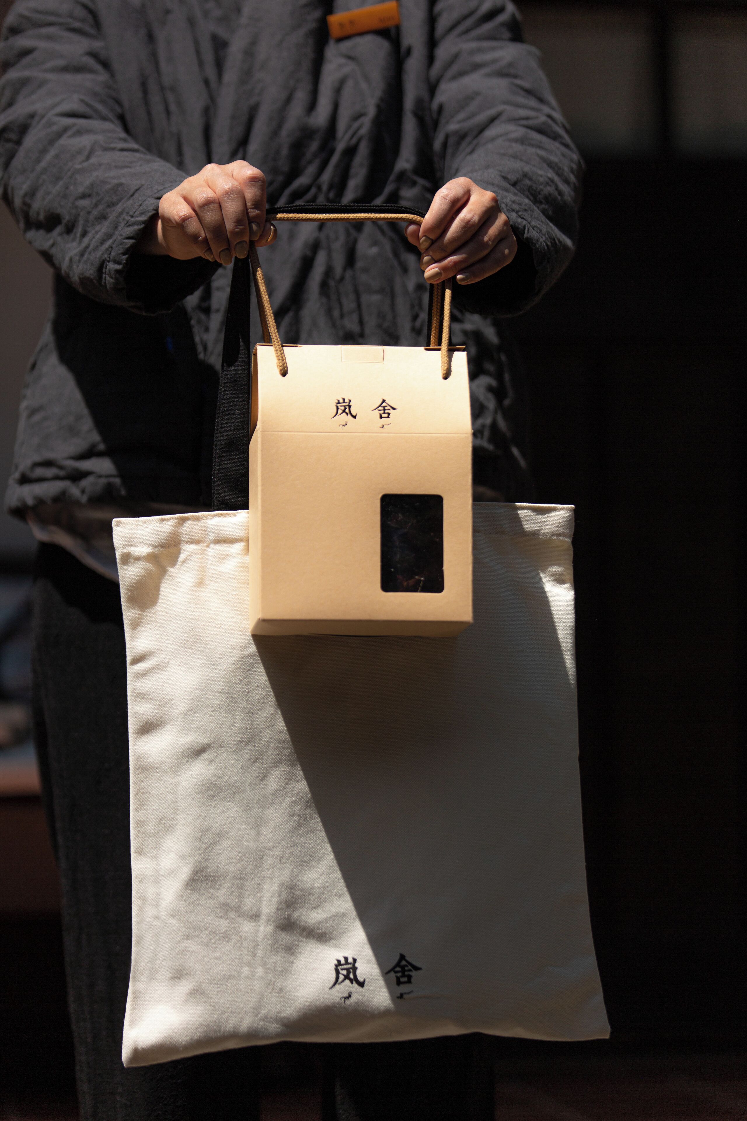 Una persona sosteniendo una bolsa de tela color beige con un bolsillo cuadrado negro y caracteres chinos.