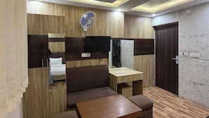 A modern room with a wooden wall panel, a flat-screen TV mounted above a sofa, a wooden coffee table, and a door with a mirror. - Hotel Beubelle (Meerut)