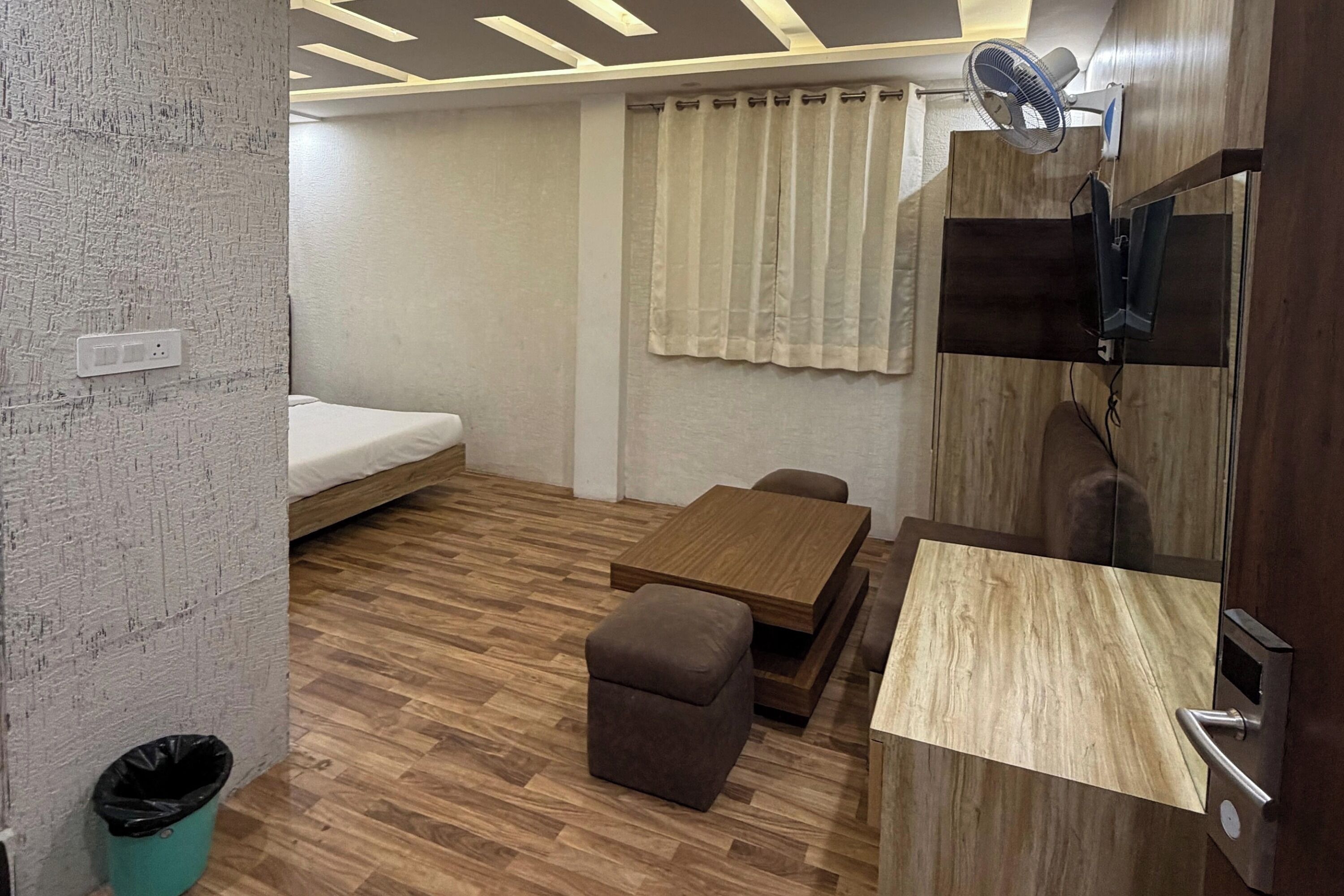 A compact room with a bed, a small table, a sofa, and a TV mounted on the wall.