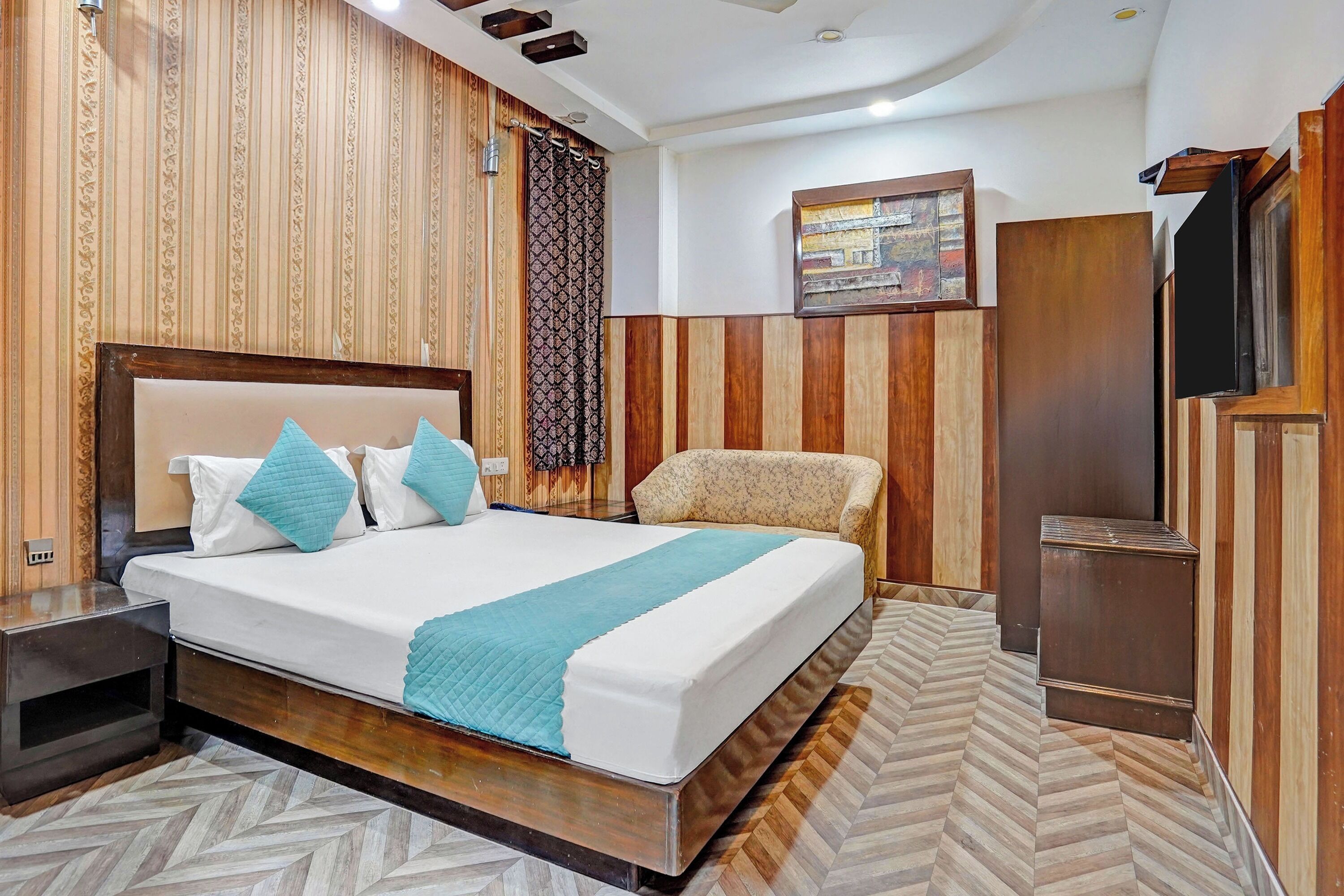 A hotel room with a large bed, a wooden headboard, a patterned curtain, a television, and a wooden wardrobe.