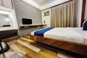 Una camera d'albergo moderna con una parete in mattoni a contrasto, una TV a schermo piatto, un letto con struttura in legno e un'ampia finestra con tende.