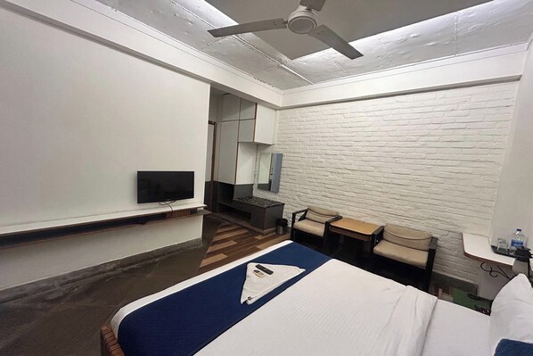A hotel room with a bed, a TV, a desk, a chair, and a white brick wall. - Premium Nest, Golf Course Road (Gurugram)
