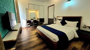 A hotel room with a bed, a desk, a chair, a TV, and a wardrobe. - Premium Nest, Golf Course Road (Gurugram)