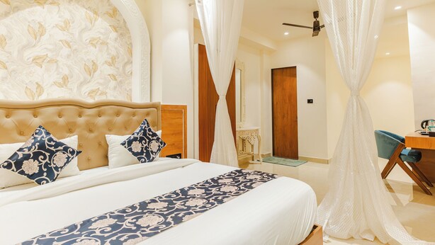A hotel room with a large bed, a wooden headboard, a desk, and a mirror. - Mahaveer Residency Hotel (Thane)