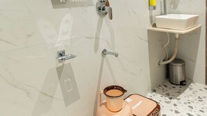 A bathroom with a marble wall, a glass shower enclosure, a sink, and a toilet. - Mahaveer Residency Hotel (Thane)