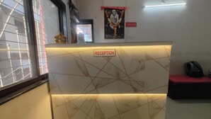 A reception area with a marble counter, a framed portrait above it, and a bench with a bag on it. - Sairam Executive (Pune)