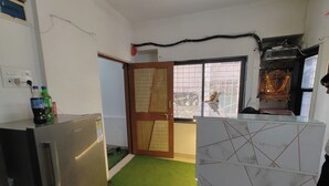 A kitchen with a refrigerator, a wooden door, and a window with a view of the outside. - Sairam Executive (Pune)