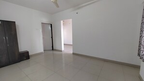 A spacious room with a ceiling fan, a wardrobe, and a door leading to another room. - Sairam Executive (Pune)