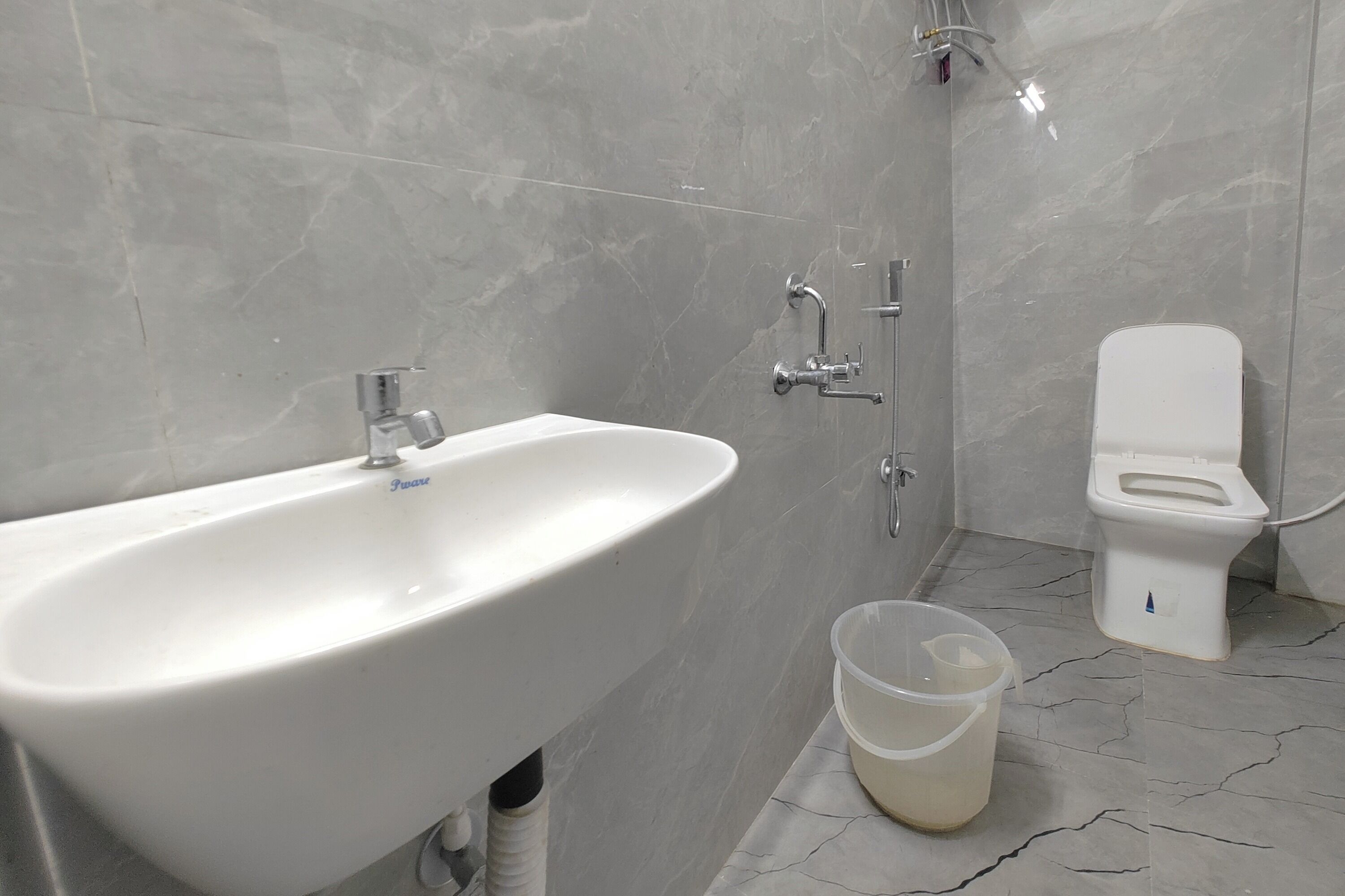 A bathroom with a white sink, a toilet, and a plastic bucket on the floor.