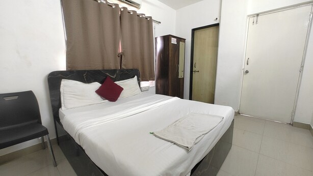 A hotel room with a bed, a wardrobe, a desk, and a chair. - Sairam Executive (Pune)