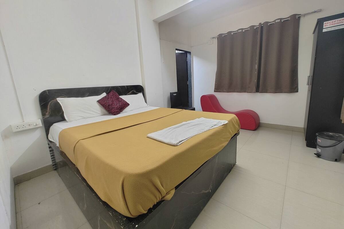 A hotel room with a bed, a red chair, a black trash bin, and a reception sign.
