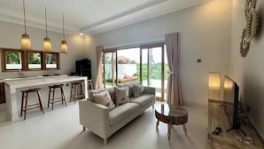 A modern living room with a sofa, a coffee table, and a kitchen area with stools. - Padi-Padi Pool Villas (Kubutambahan)