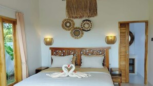 A bedroom with a bed, two bedside tables, a wooden headboard, wall decor, and a door leading to another room. - Padi-Padi Pool Villas (Kubutambahan)