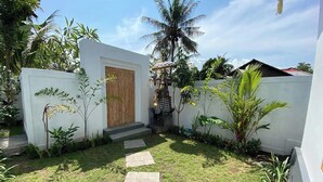 A well-maintained garden with a wooden door, a small statue, and a palm tree. - Padi-Padi Pool Villas (Kubutambahan)
