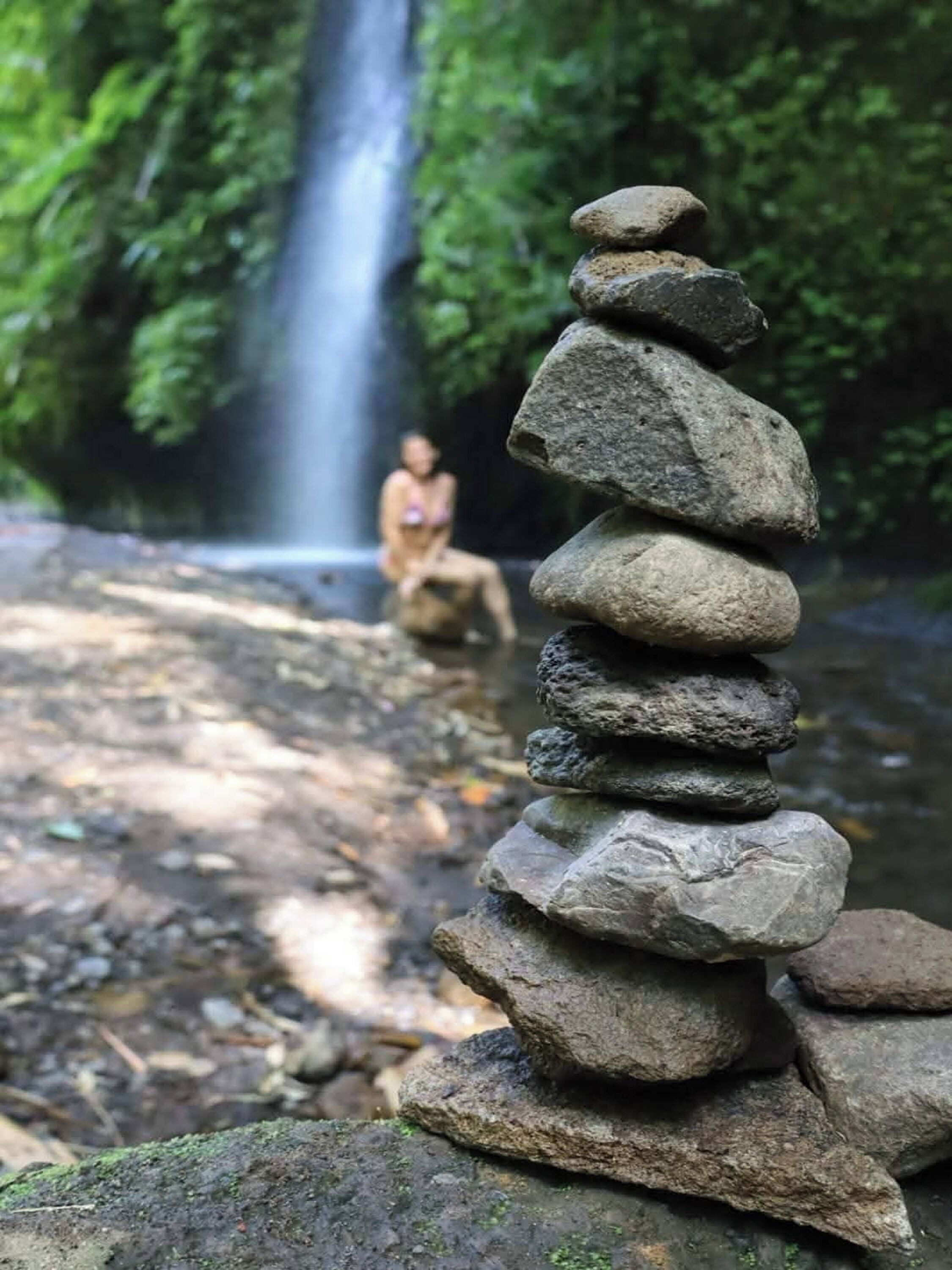 A stack of stones in a forested area with a waterfall in the background.