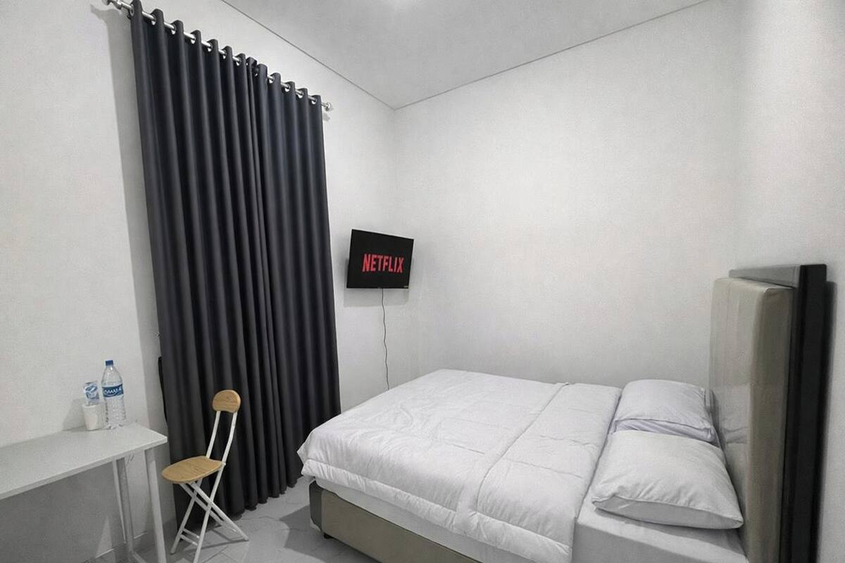 A bedroom with a bed, a TV mounted on the wall, a desk with a chair, and a water bottle on the desk.