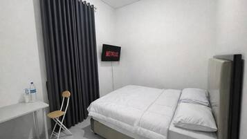 Une chambre avec un lit, un téléviseur fixé au mur, un bureau avec une chaise et une bouteille d’eau sur le bureau.