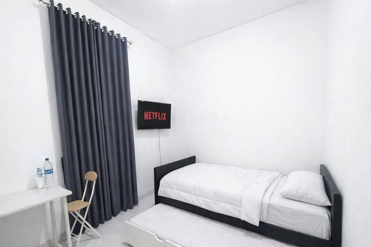 A small, modern room with a bed, a desk, a chair, and a TV displaying 'NETFLIX'.