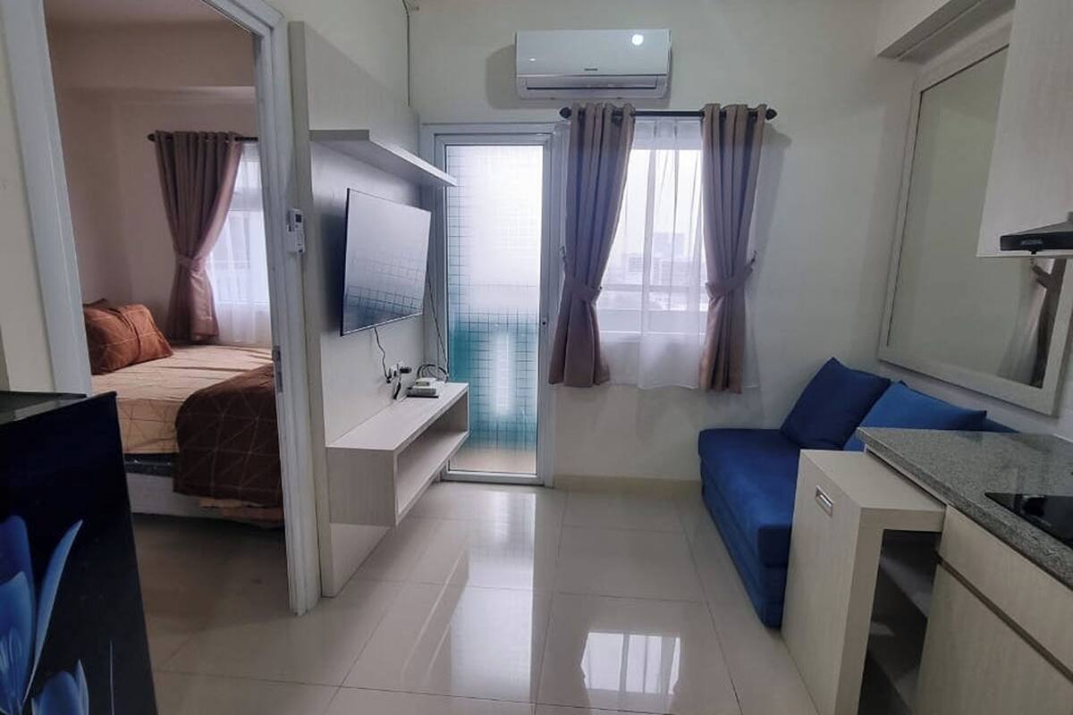 A modern, compact living space with a bed, a blue sofa, a small kitchenette, and a TV.