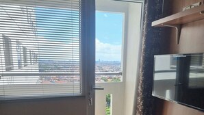 A room with a large window, a door, and a mounted flat-screen TV. - Apartemen Green Pramuka City By Rizal Properti (Jakarta)