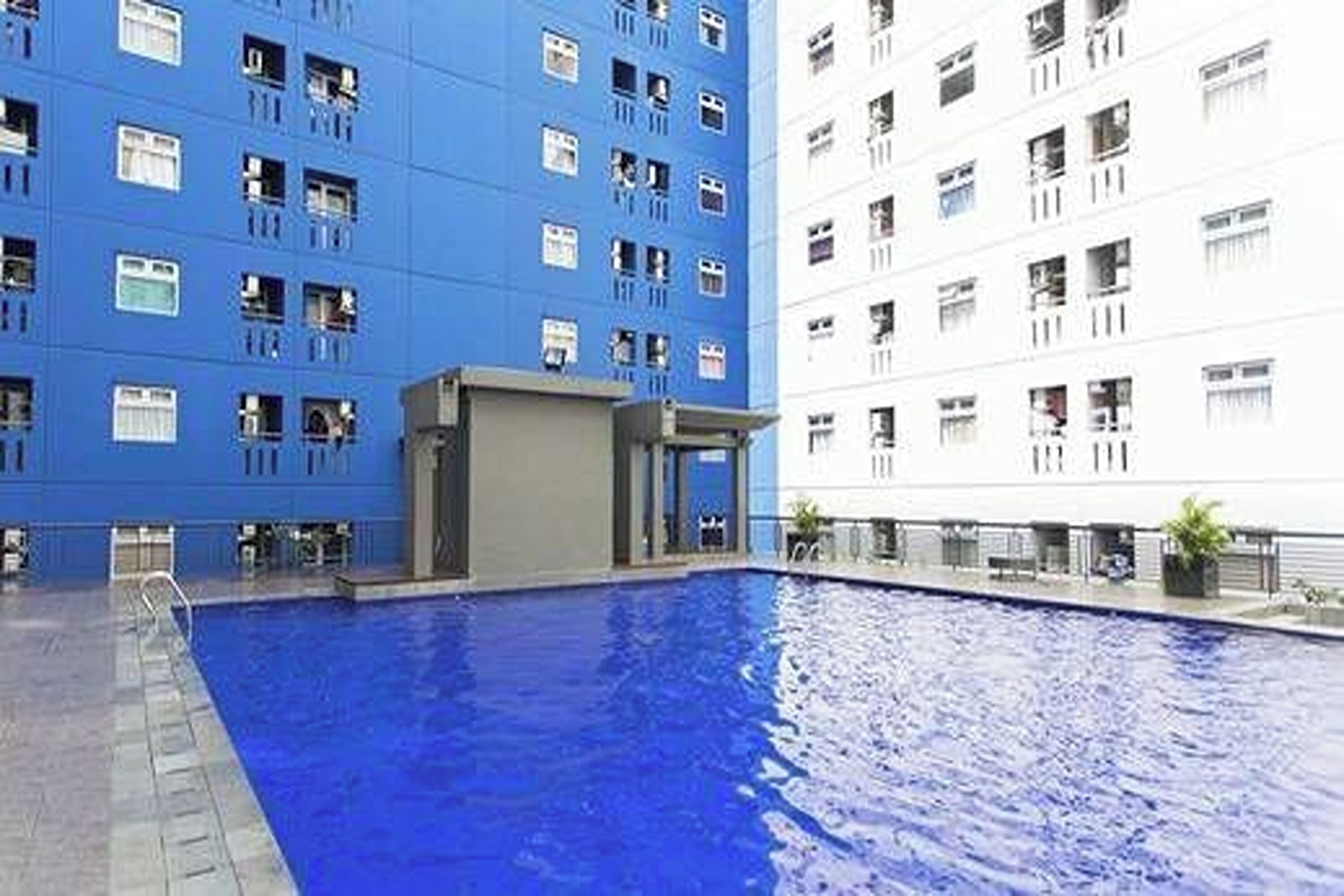En swimmingpool med ett blått kakelbeklätt poolområde, omgiven av en byggnad med en blå fasad och en vit byggnad med en vit fasad.