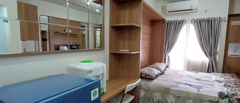A bedroom with a bed, a desk, a mirror, and a wardrobe.
