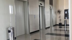 A clean, modern lobby with a checkered floor, a trash bin, and a potted plant. - Apartemen Green Pramuka City By Rizal Properti (Jakarta)