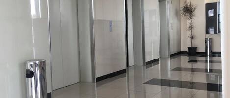 A clean, modern lobby with a checkered floor, a trash bin, and a potted plant.