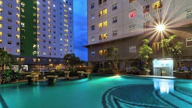 A swimming pool with a circular pattern, surrounded by buildings with illuminated windows. - Apartemen Green Pramuka City By Rizal Properti (Jakarta)