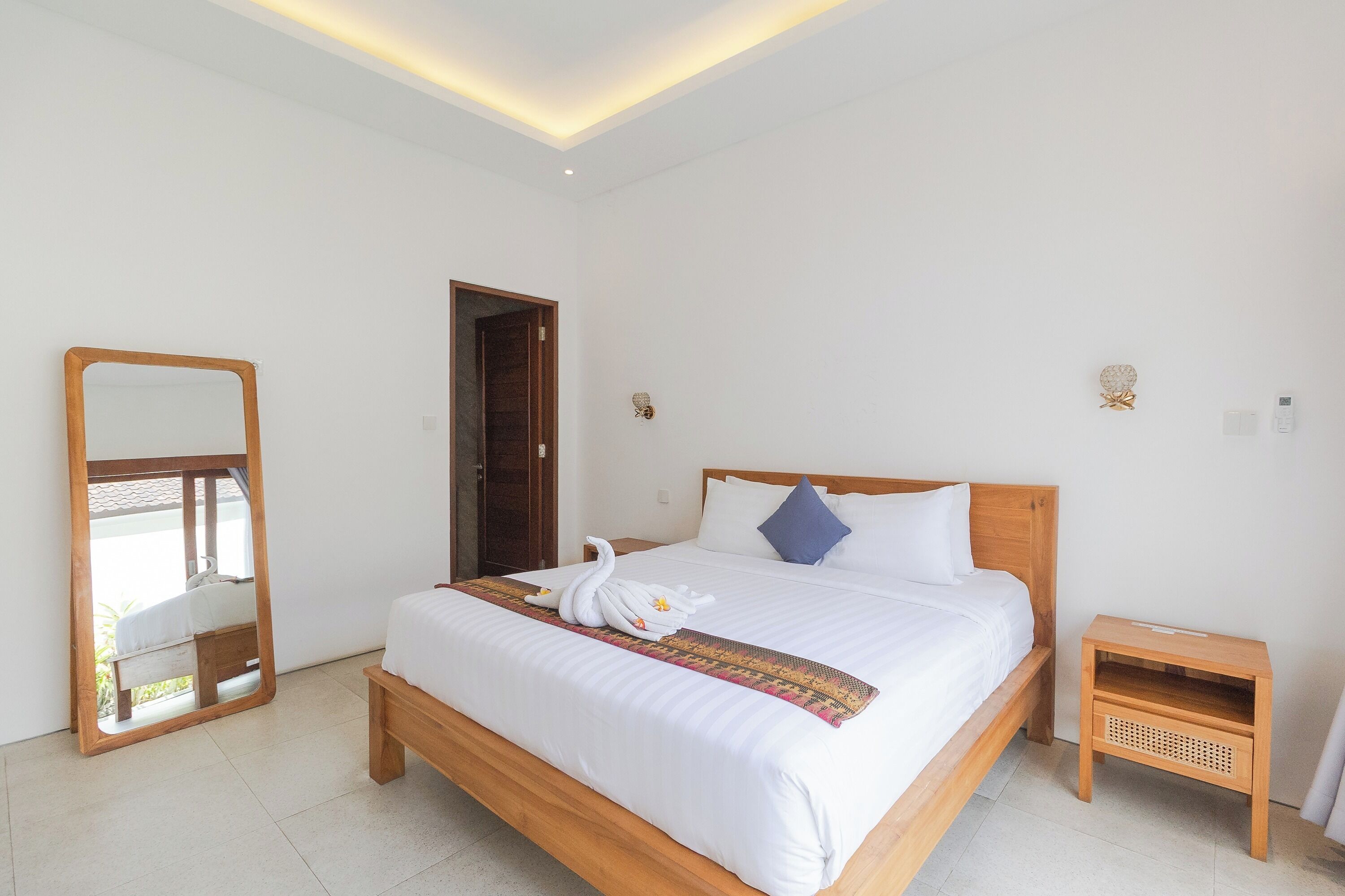 Una camera d'albergo con un letto grande, un comodino in legno, uno specchio e una porta.
