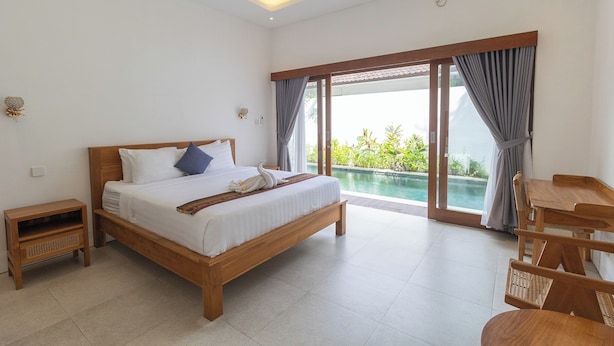 Un dormitorio con una cama de madera, una mesita de noche, una mesa de comedor con sillas y vistas a una piscina exterior.
