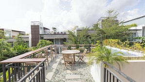 Terraza en la azotea con mobiliario exterior, una pequeña mesa y abundante vegetación.