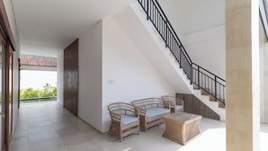 Amplio espacio interior con una escalera, muebles de mimbre y vistas al exterior con vegetación.
