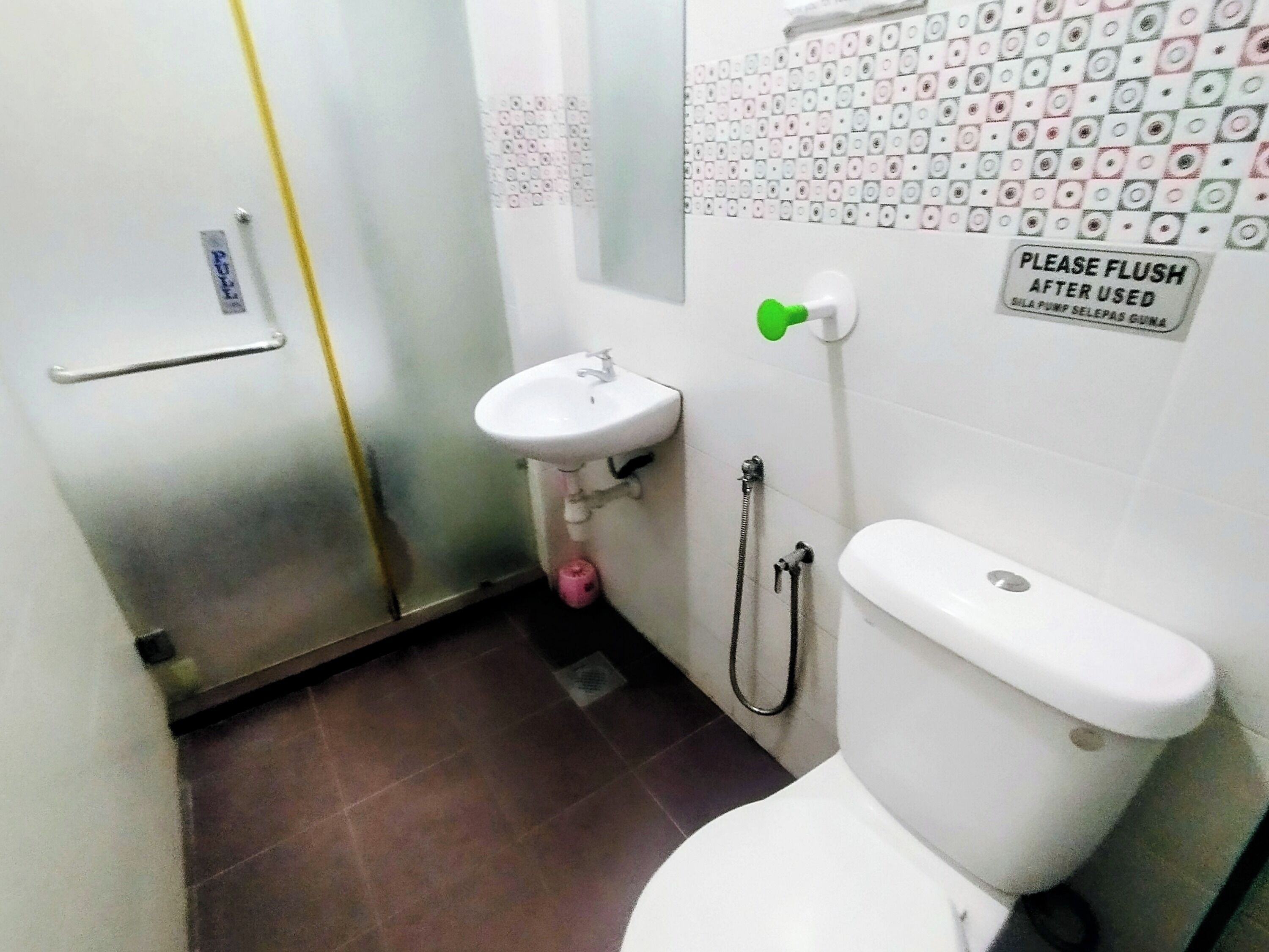 A small bathroom with a toilet, sink, and shower. There is a sign on the wall that says "PLEASE FLUSH AFTER USED".