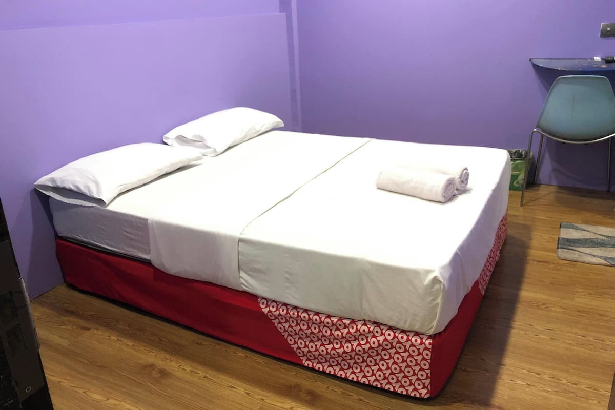 A single bed with white bedding, a red and white patterned skirt, and a blue chair in a room with purple walls.