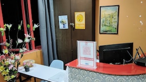 A reception desk with a patterned curtain, a framed picture of a cityscape, and a vase with flowers on a table. - Cahaya Hanson (Bilikxpert) (Kuala Lumpur)