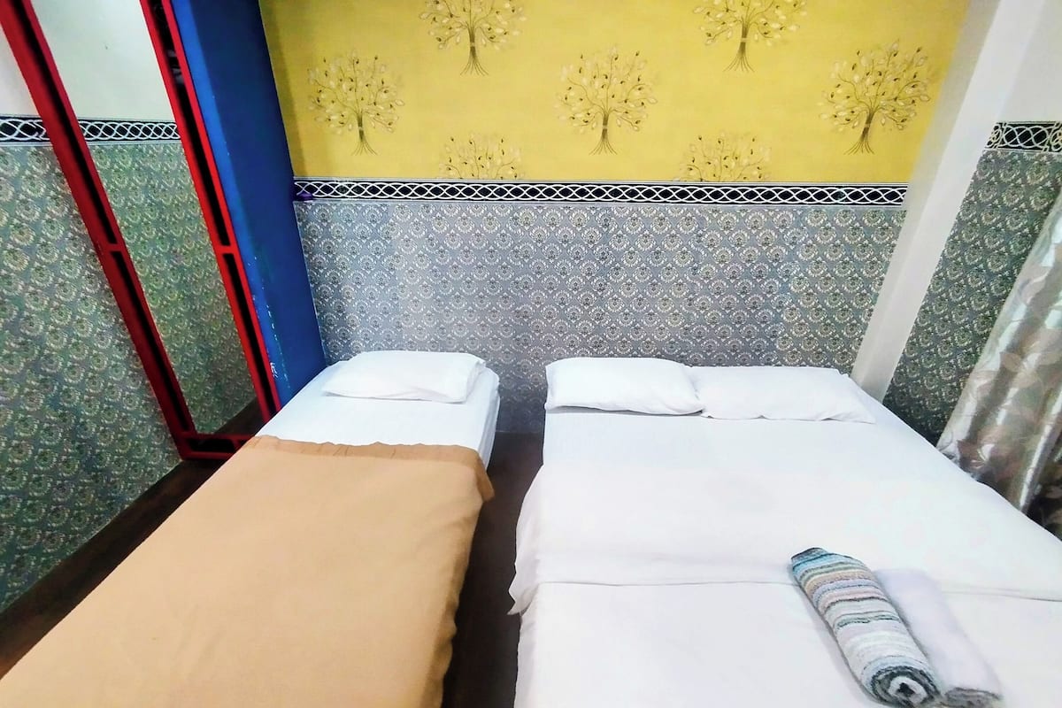 A room with two single beds, each with a white mattress and a brown blanket.
