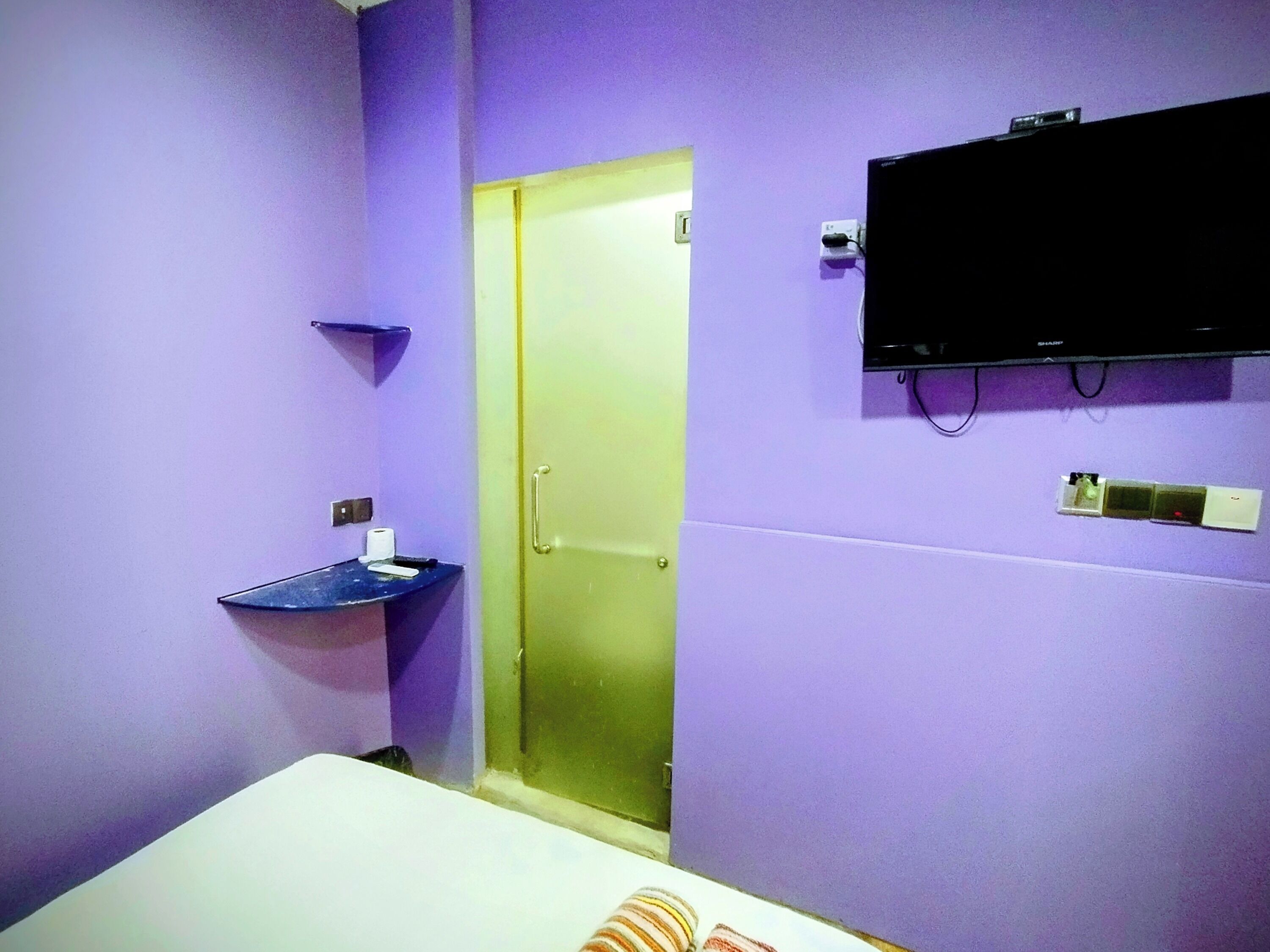 A room with a bed, a small sink, a television mounted on the wall, and a door leading to another room.