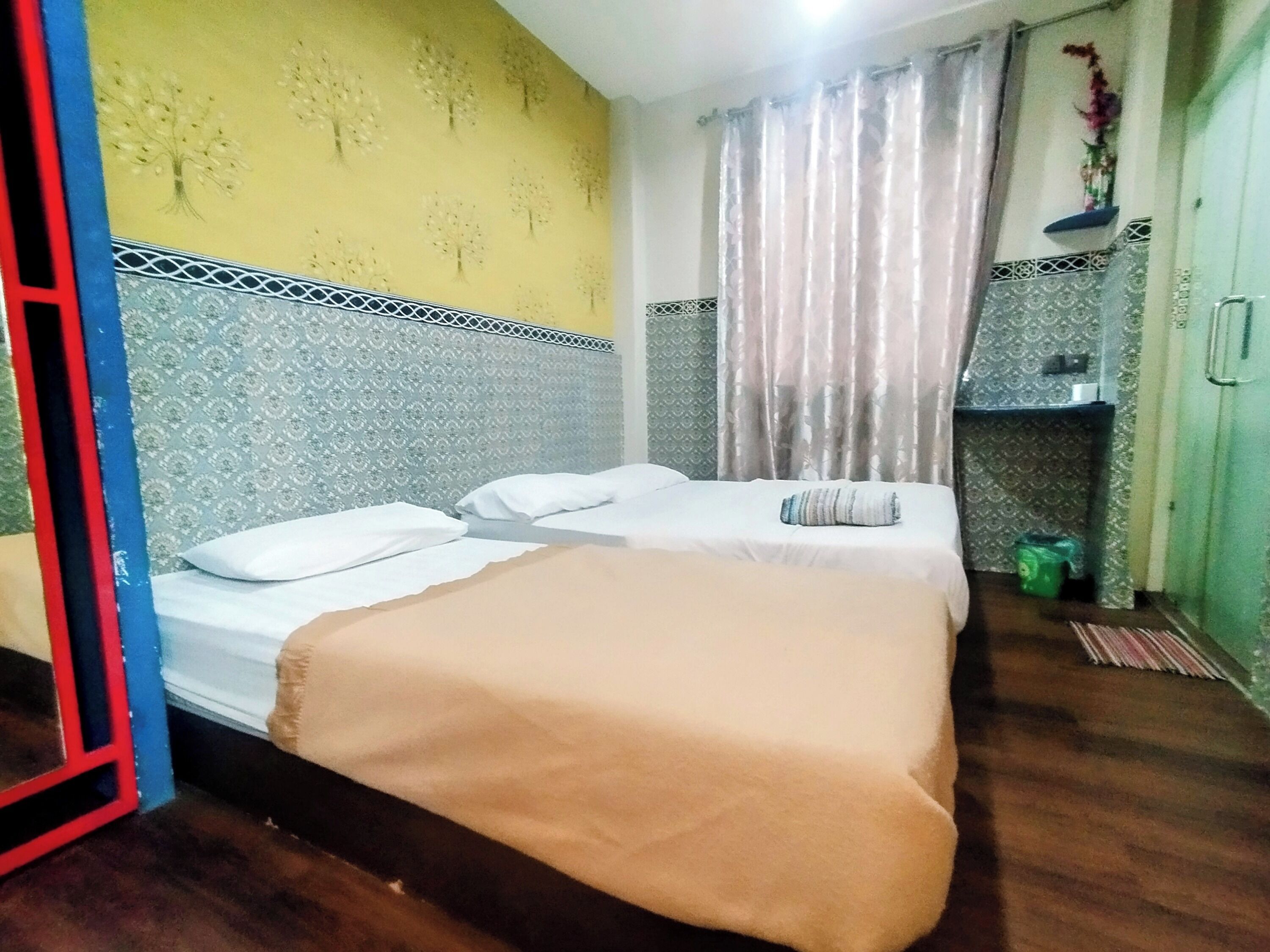 A hotel room with two beds, a patterned headboard, a yellow wall with tree designs, and a green trash bin.