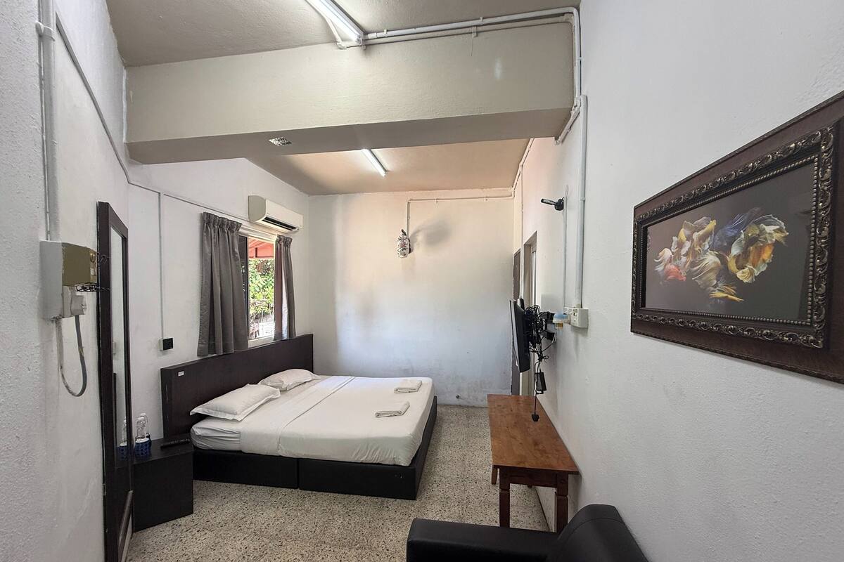A compact hotel room with a bed, bedside table, a small wooden table, a mirror, and a framed picture on the wall.