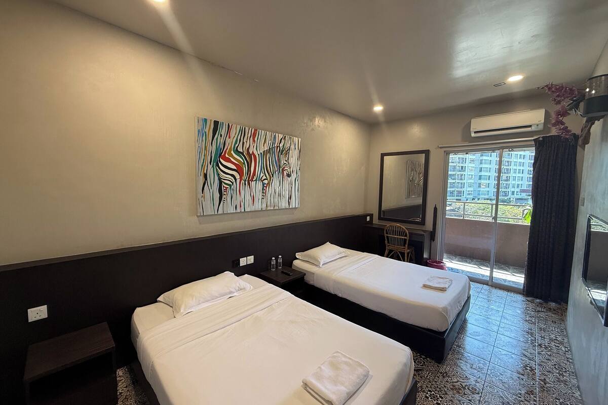 A hotel room with two beds, a desk, a chair, a large abstract painting, and a view of the outside.