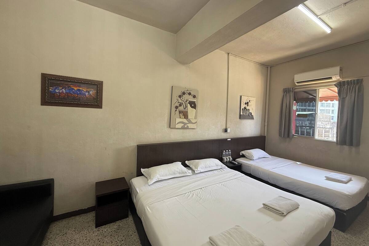 A hotel room with two beds, a nightstand, a wall-mounted air conditioner, and a window with curtains.