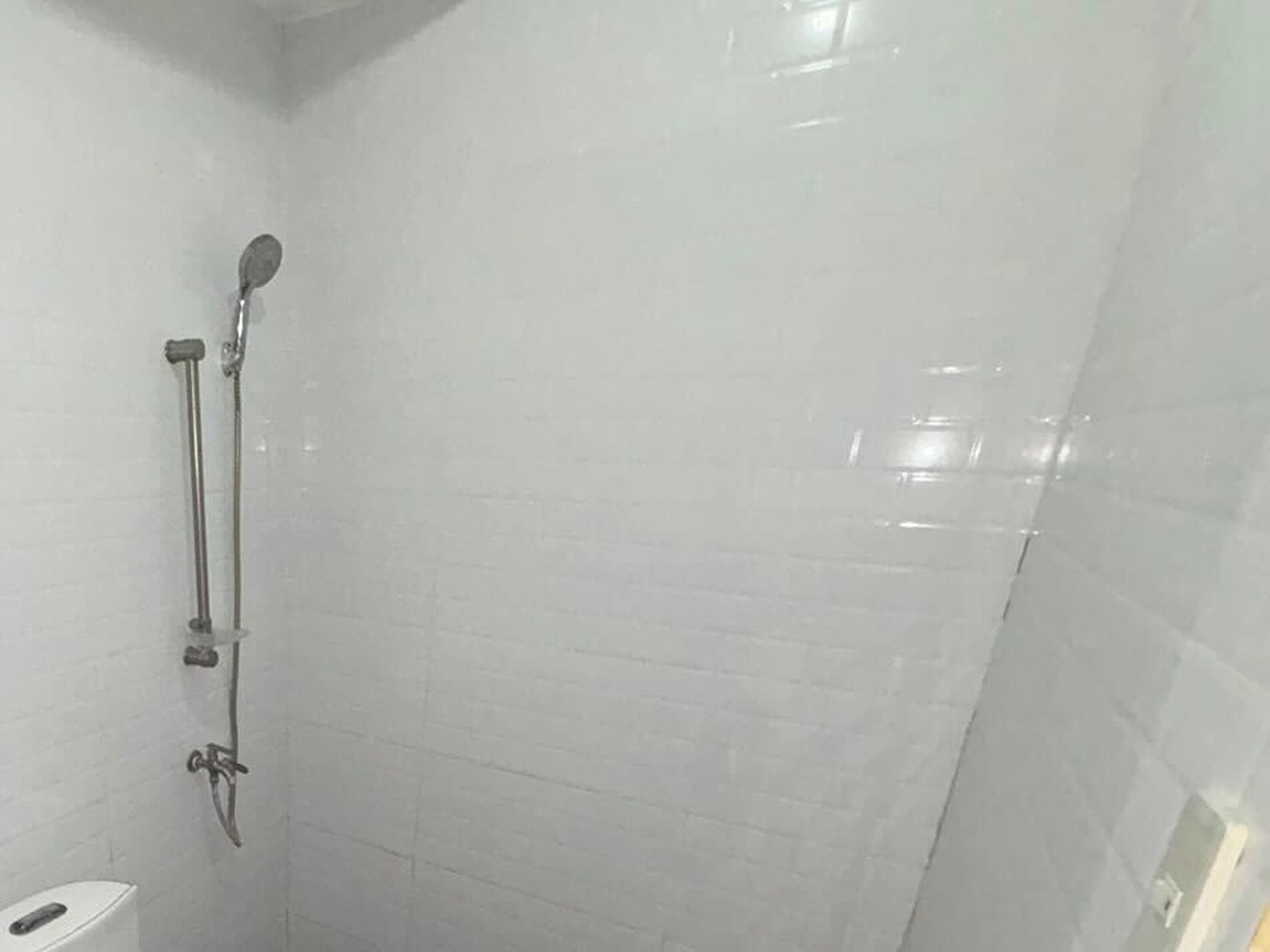 A bathroom with white tiled walls, a shower with a handheld showerhead, and a toilet.