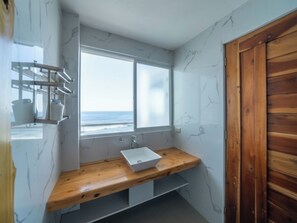 A bathroom with a wooden vanity, a white sink, and a window overlooking the ocean. - Turtle Beach Resort (San Juan)