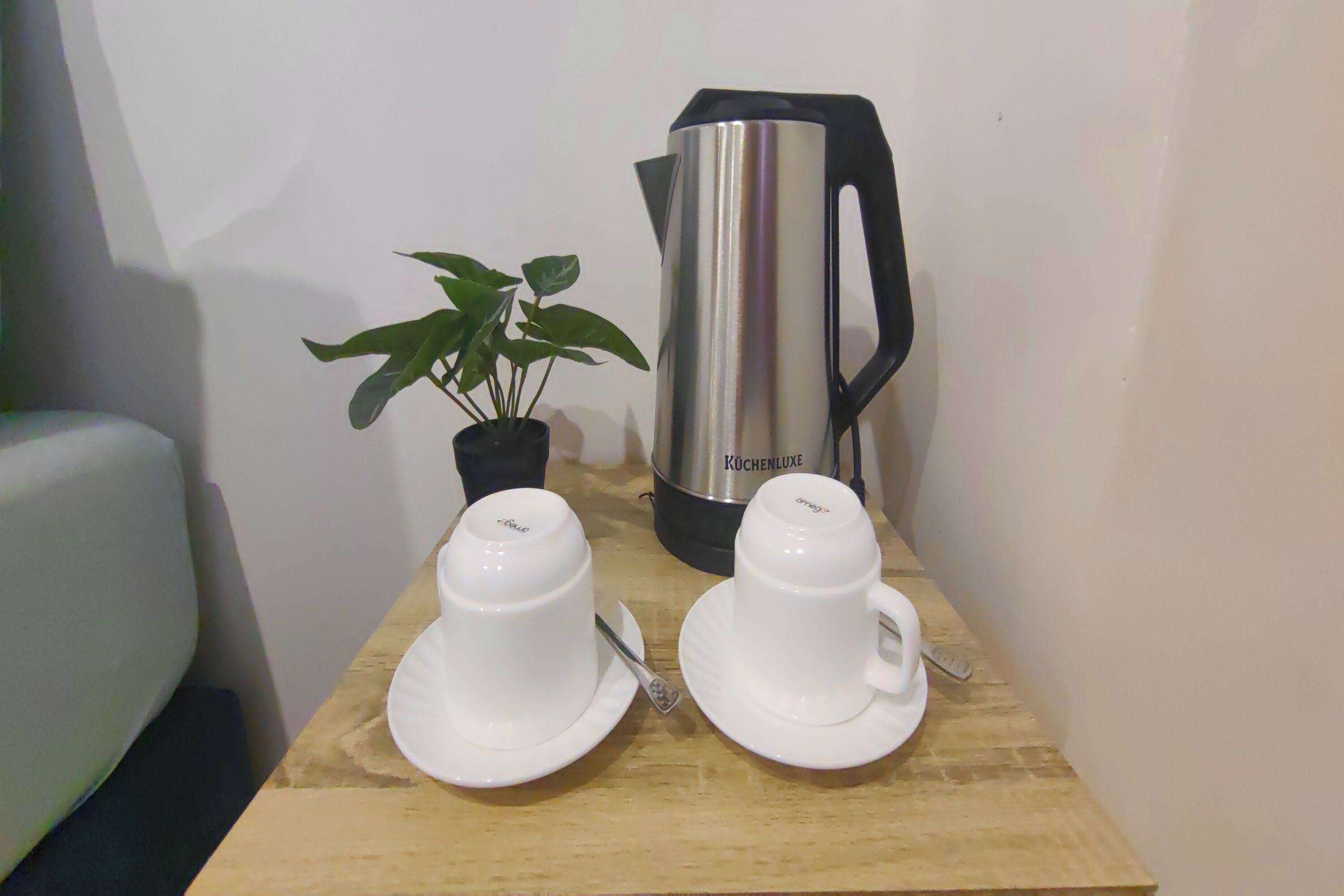 A wooden table with two white cups and saucers, a black kettle, and a potted plant.