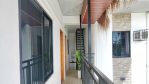 A narrow corridor with a wooden door, a staircase, and a view of a room with a window and a plant. - Eva'S Guest House (General Luna)