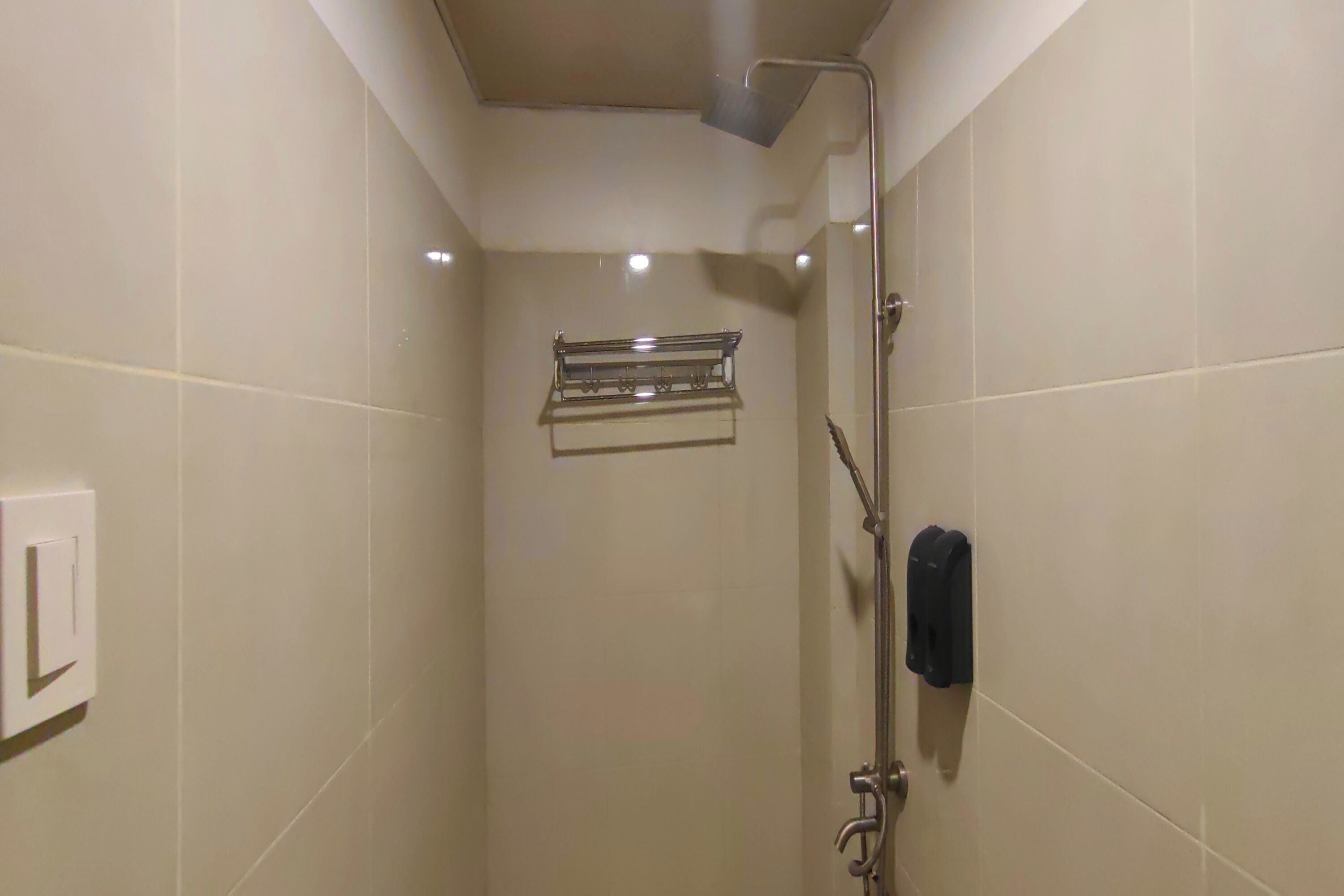Un petit espace de douche carrelé, équipé d’un pommeau de douche à main, d’un porte-serviettes et d’un distributeur de savon.